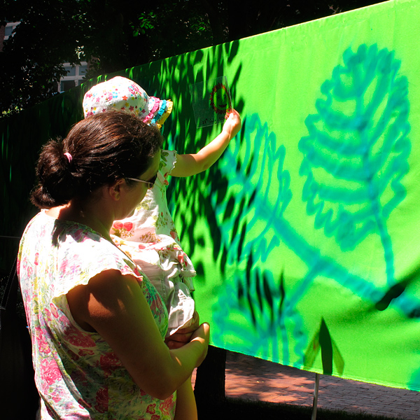 mother holding baby up to large cartoon leaves painted on green fabric, Wharf District Parks, Boston