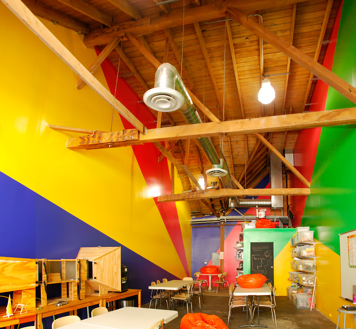 forced perspective paint design, triangulating walls in bright yellow, navy, pinkish-red and bright green, in kids STEM after-school studio, Iridescent, LA