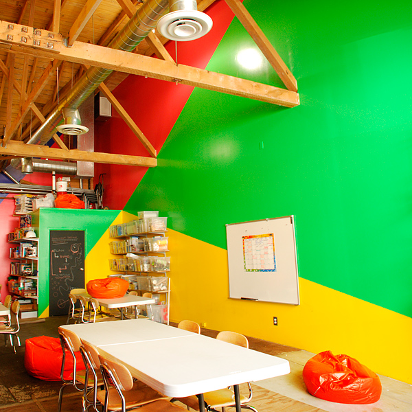 forced perspective paint design, triangulating walls in bright yellow, pinkish-red and bright green, in kids STEM after-school studio, Iridescent, LA
